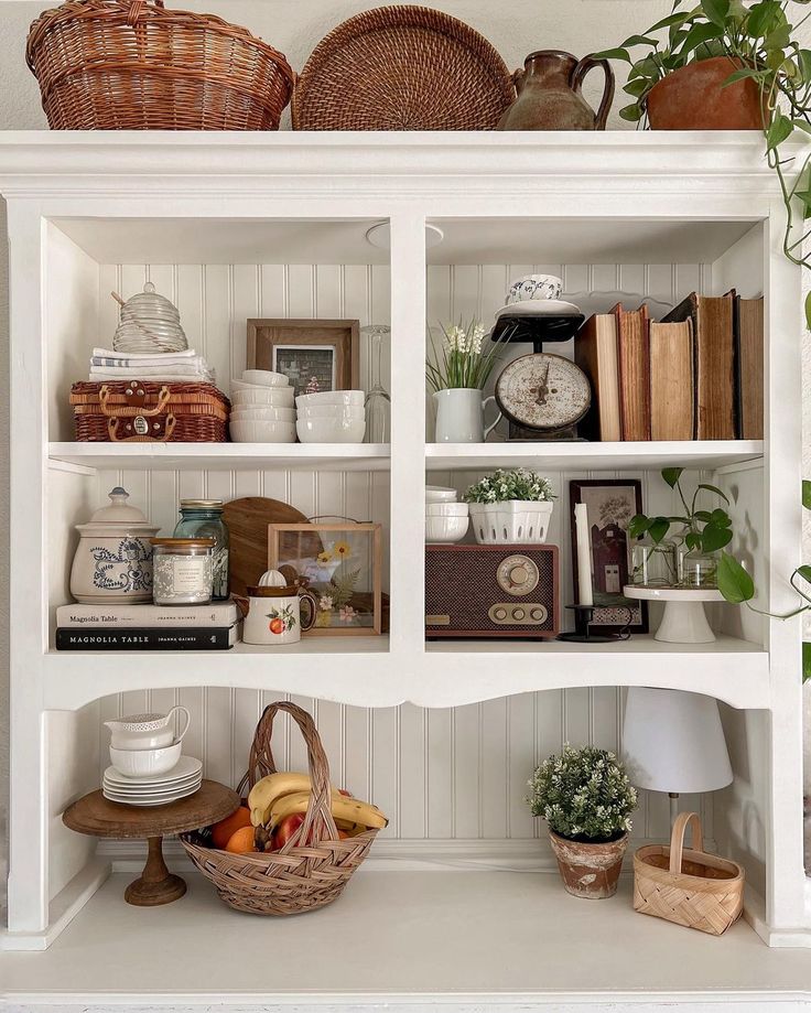 a white bookcase filled with lots of books next to a potted plant and other items