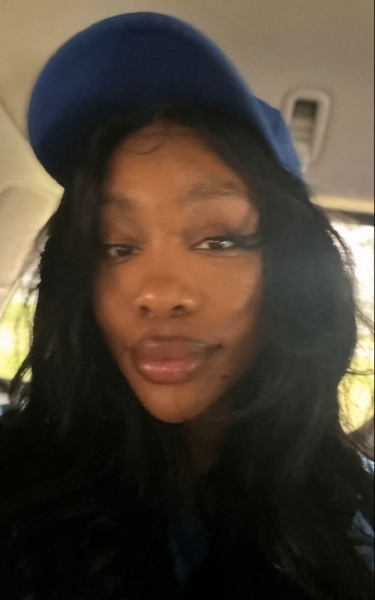 a woman wearing a blue hat in the back seat of a car, looking at the camera