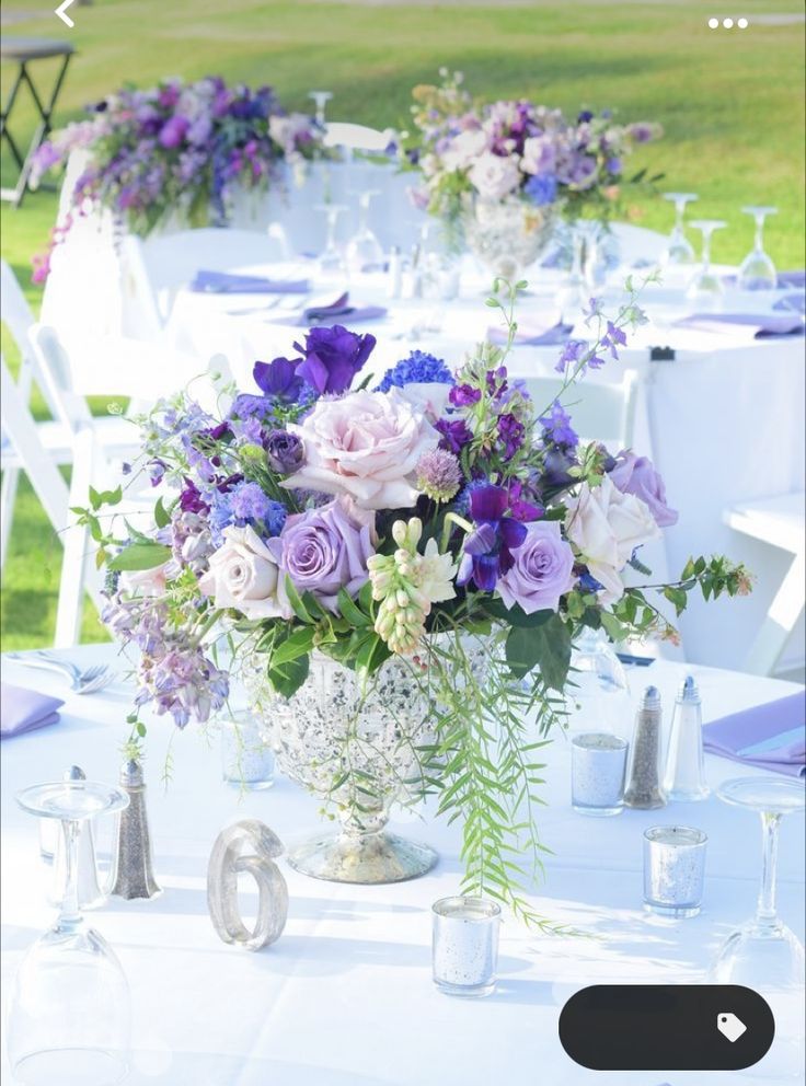 a vase filled with purple and white flowers on top of a table next to chairs