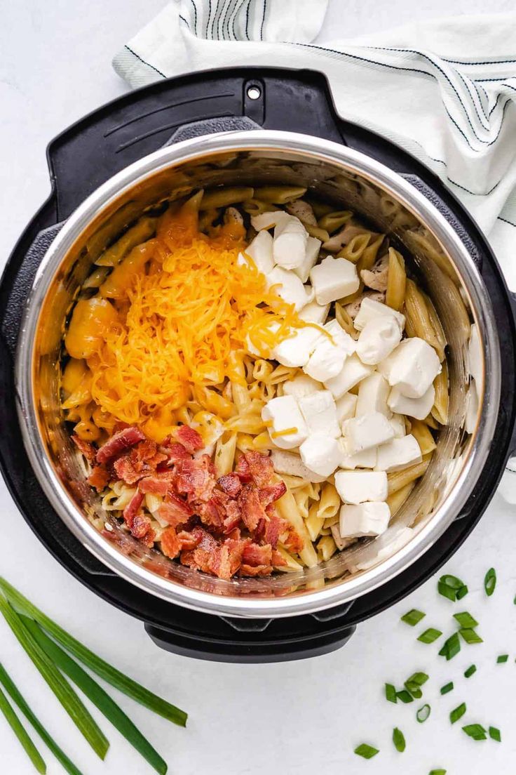 an overhead view of pasta and cheese in the crock pot with green onions on the side