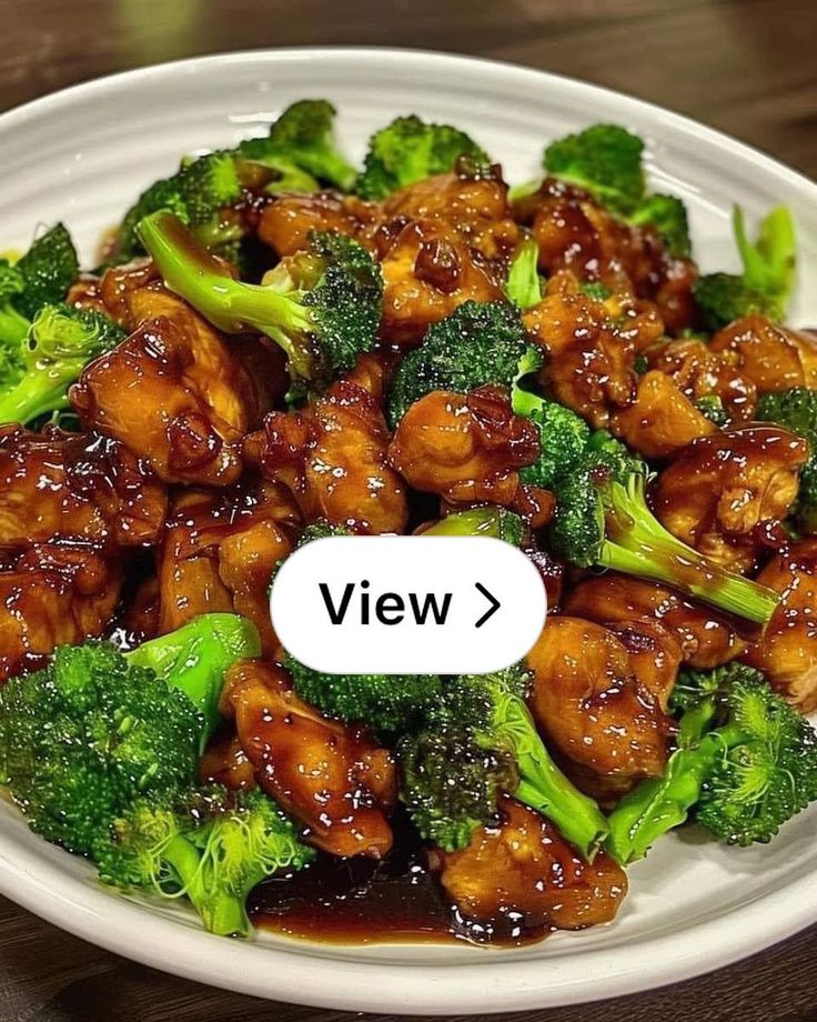 a white plate topped with chicken and broccoli on top of a wooden table