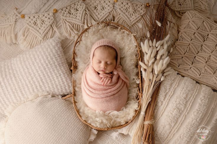 a newborn baby wrapped in a pink blanket laying on top of a bed next to pillows