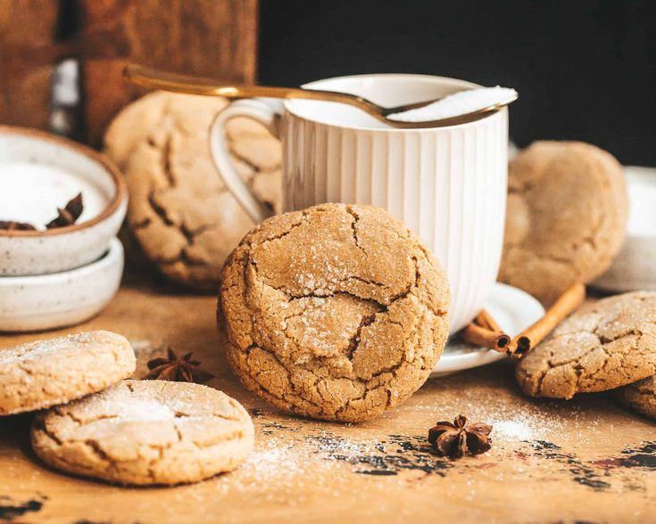 some cookies are sitting on a table next to a cup and saucer with cinnamon sticks