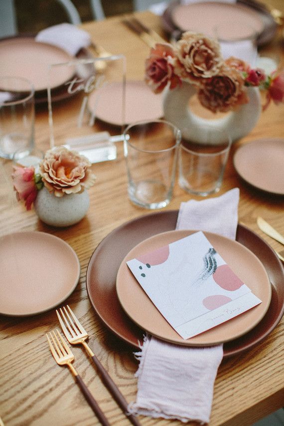 the table is set with pink plates and silverware, napkins and flowers in vases