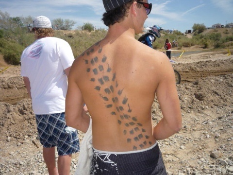 a man with his back turned to the camera, wearing a towel and showing tattoos on his chest