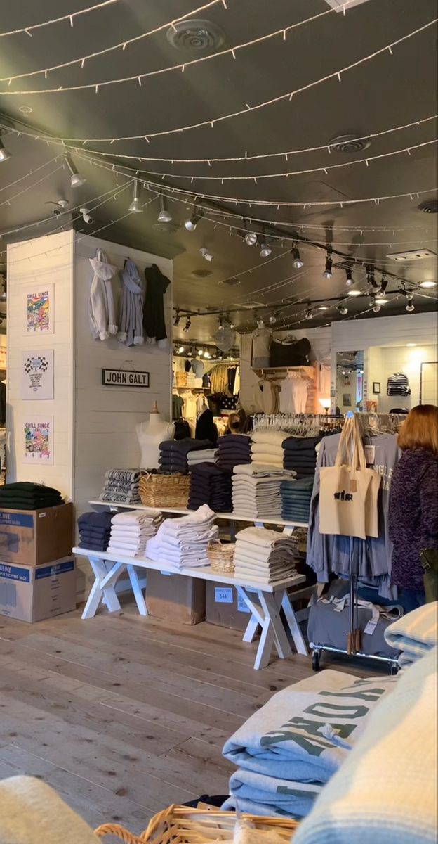 the inside of a clothing store with lots of clothes on tables and lights hanging from the ceiling