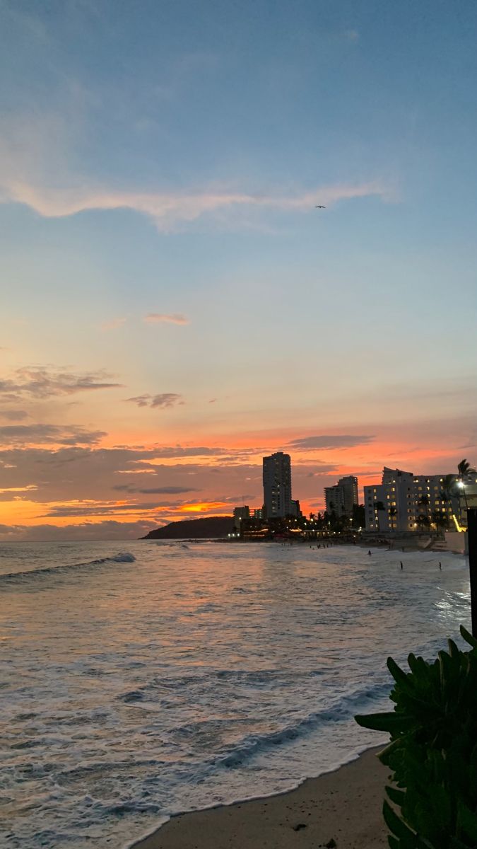 the sun is setting over the ocean with buildings in the background