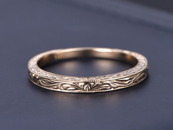 an antique style wedding band with intricate engraving on the side, sitting on a black surface