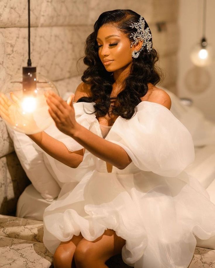 a woman sitting on a bed holding a lit candle in her hand and wearing a white dress