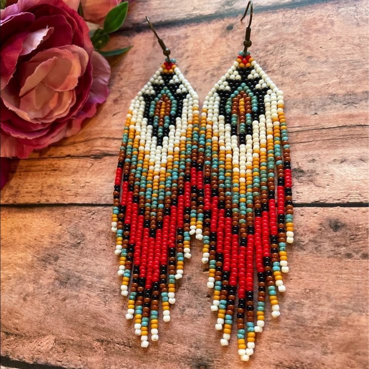 two pairs of beaded earrings sitting on top of a wooden table next to flowers