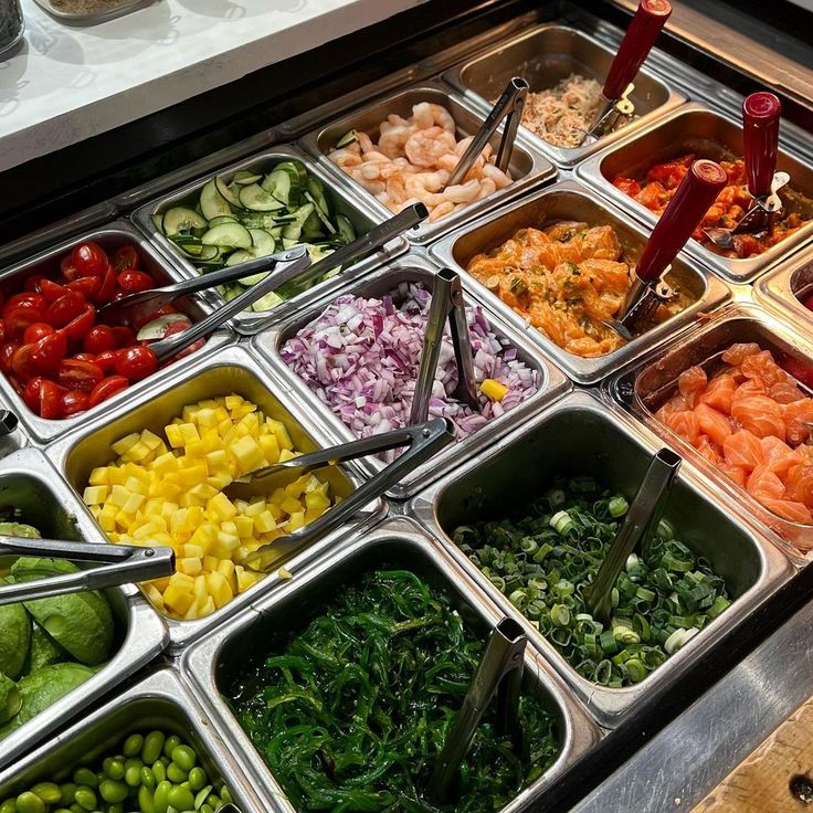 an assortment of different types of vegetables in trays on a buffet table with utensils