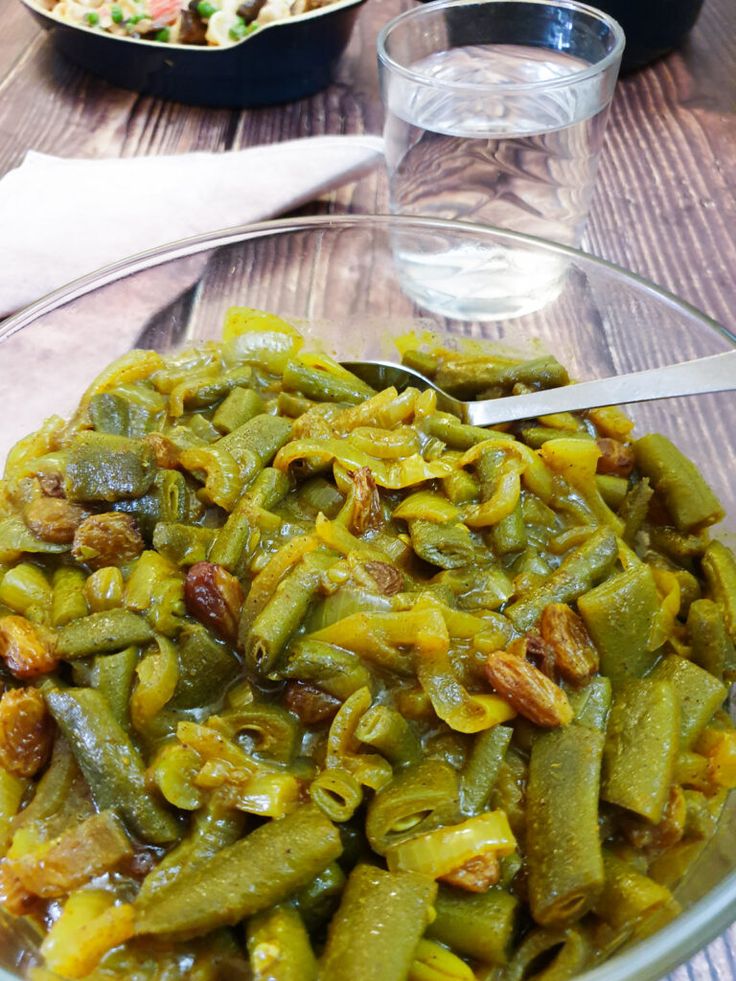 a glass bowl filled with green beans on top of a table next to a plate of food