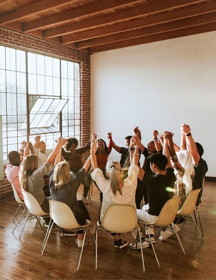 a group of people sitting in chairs holding their hands up to the sky with one person standing