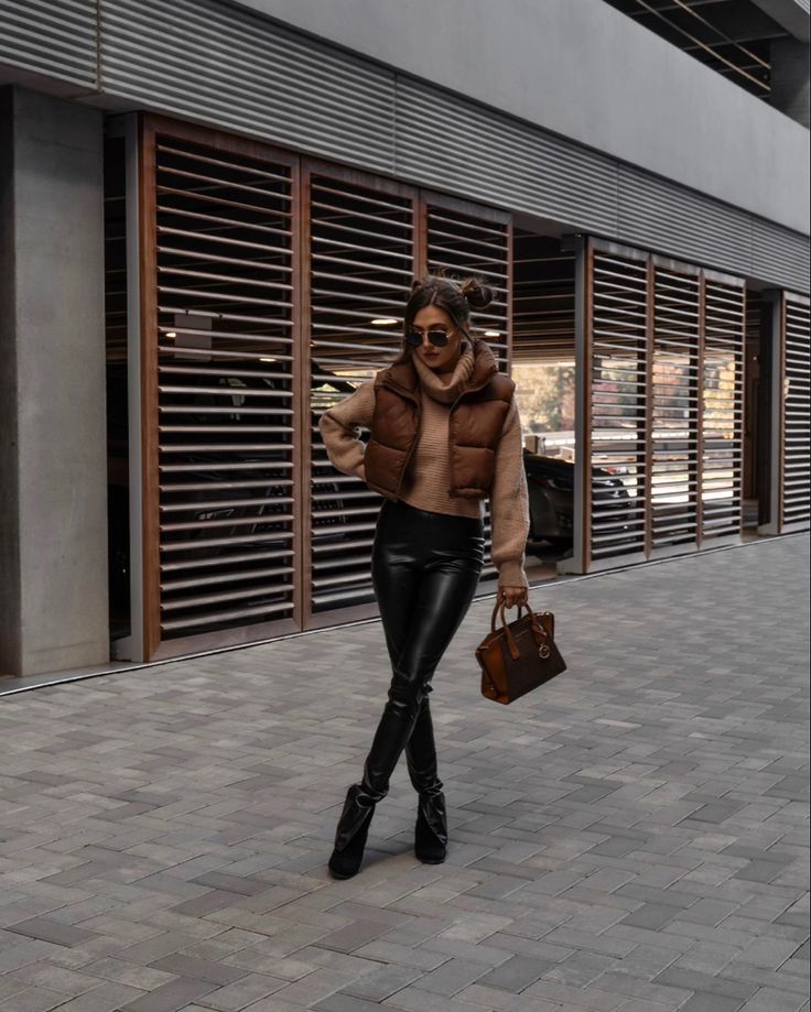 Brown puffer vest, beige cowl neck sweater, black leather pants streetstyle outfit Brown Puffer Outfit, Space Buns Outfit, Brown Puffer Vest Outfit, Brown Vest Outfit, Winter Vest Outfits, Vest Outfits Aesthetic, Winter Layering Outfits, Puffer Outfit, Puffer Vest Outfit