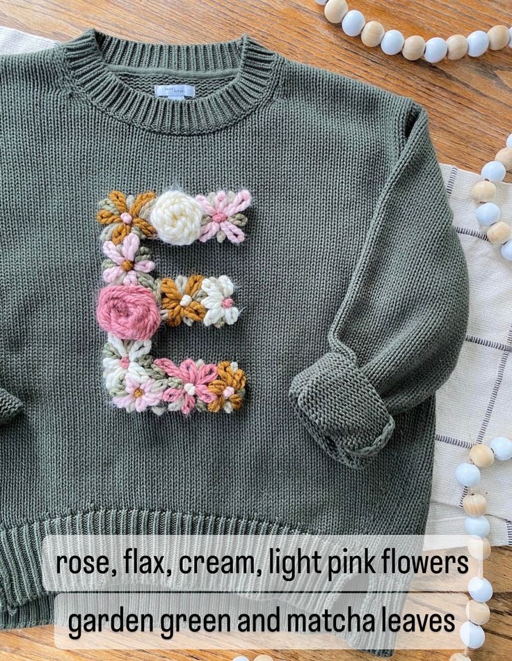 a green sweater with flowers on it and the letter e written in crochet