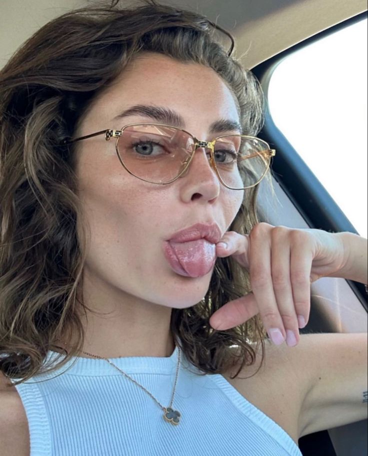 a woman sticking her tongue out in the back seat of a car while wearing glasses