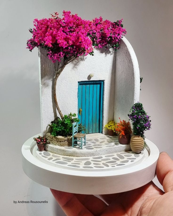 there is a miniature house with pink flowers on the front and blue door in the back