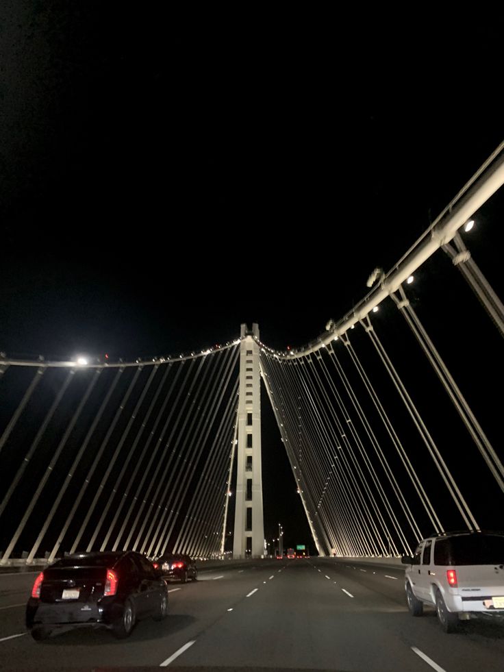 cars driving across a bridge at night with lights shining on the top and bottom part