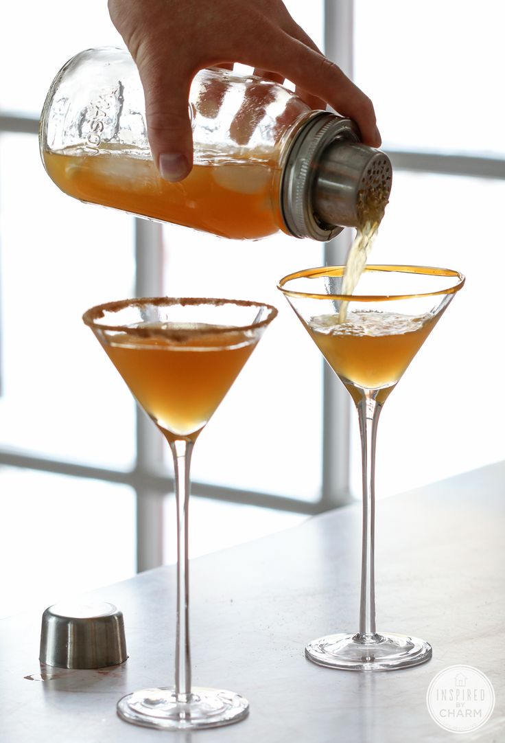 a person pours an alcoholic drink into two martini glasses