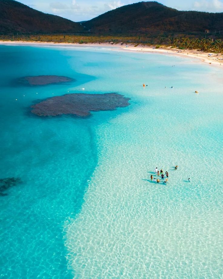 people on surfboards in shallow blue water near an island with white sand and corals