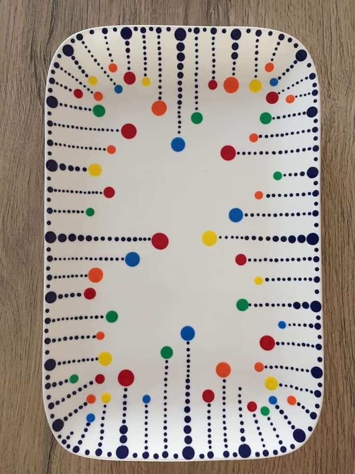 a white plate with multicolored dots and lines on the edge, sitting on a wooden surface