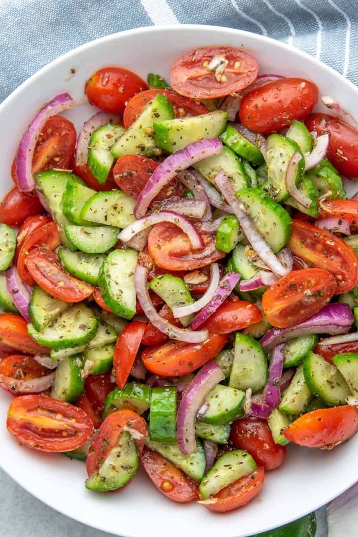 a white bowl filled with cucumber, onion and tomato salad on top of a table