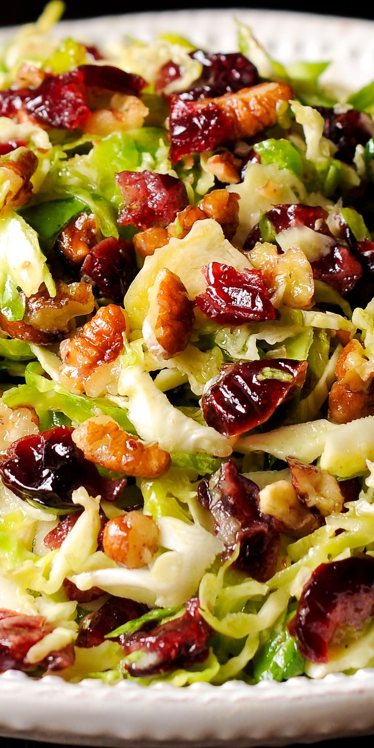 a salad with cranberries, lettuce and nuts in it on a white plate