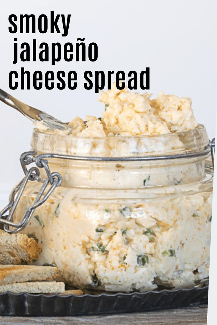 a glass jar filled with cheese and crackers on top of a wooden table next to bread