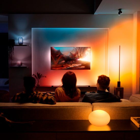 two people sitting on a couch in front of a television with an orange and blue light