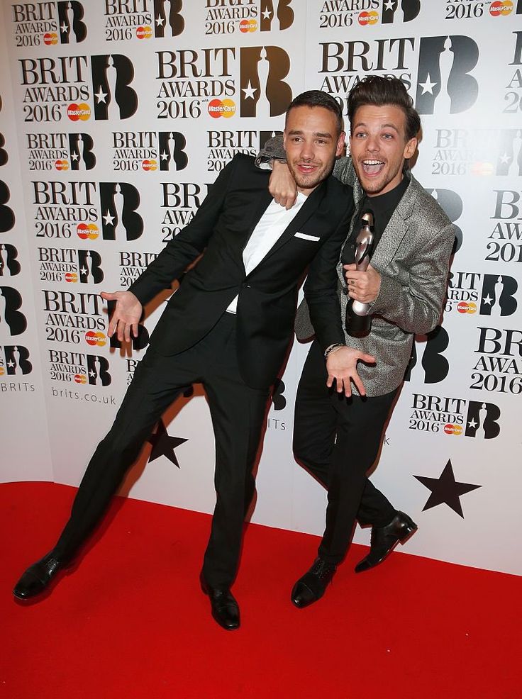 two men in suits posing on the red carpet at the brity awards, with one holding