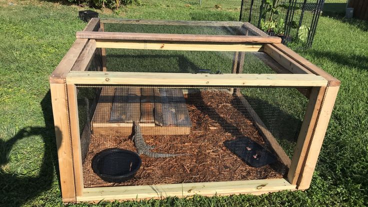 a wooden box with a chicken in it sitting on the grass next to a fence