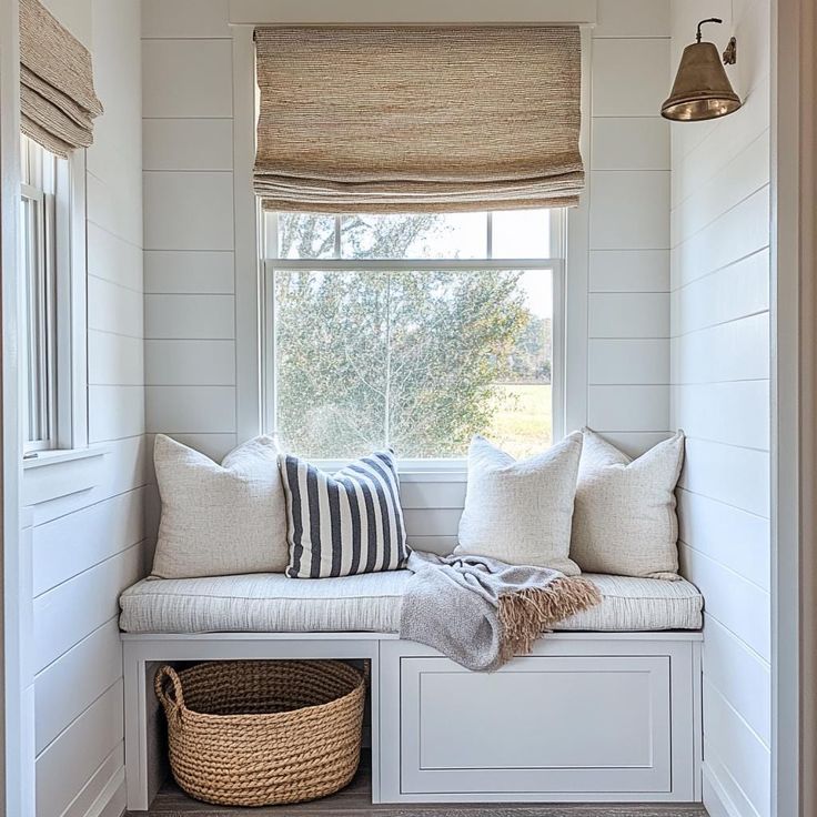 a window seat with pillows and blankets on it next to a basket under the window