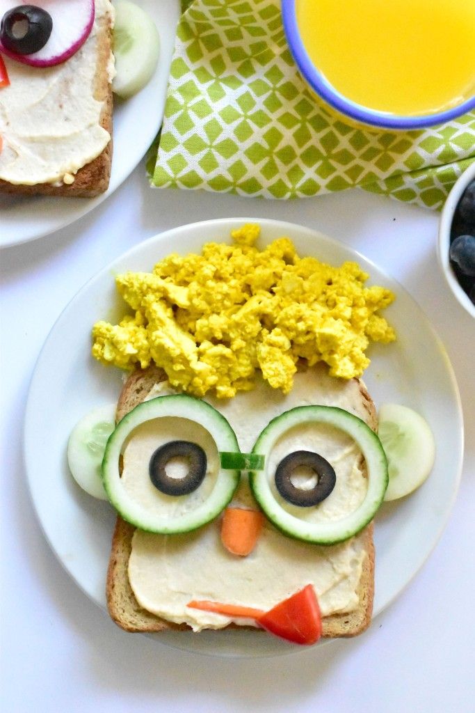 a plate topped with an owl face sandwich next to blueberries and cucumbers