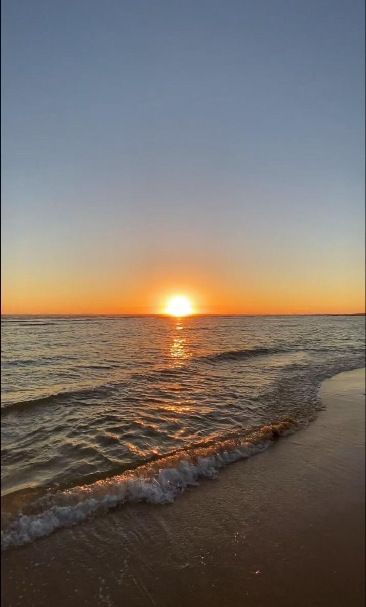 the sun is setting over the water at the beach with waves coming in to shore