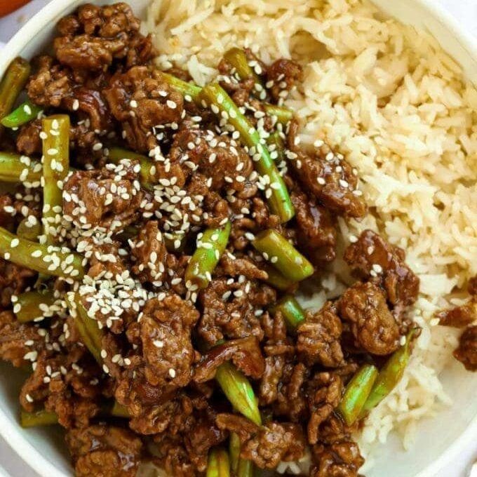 a white bowl filled with meat and asparagus on top of rice next to an orange napkin