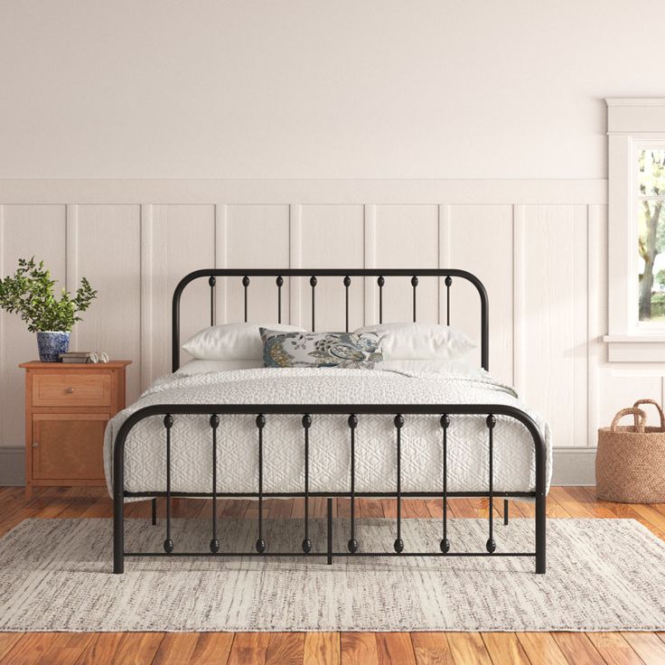 a bedroom with white walls and wood flooring has a black iron bed frame on the side