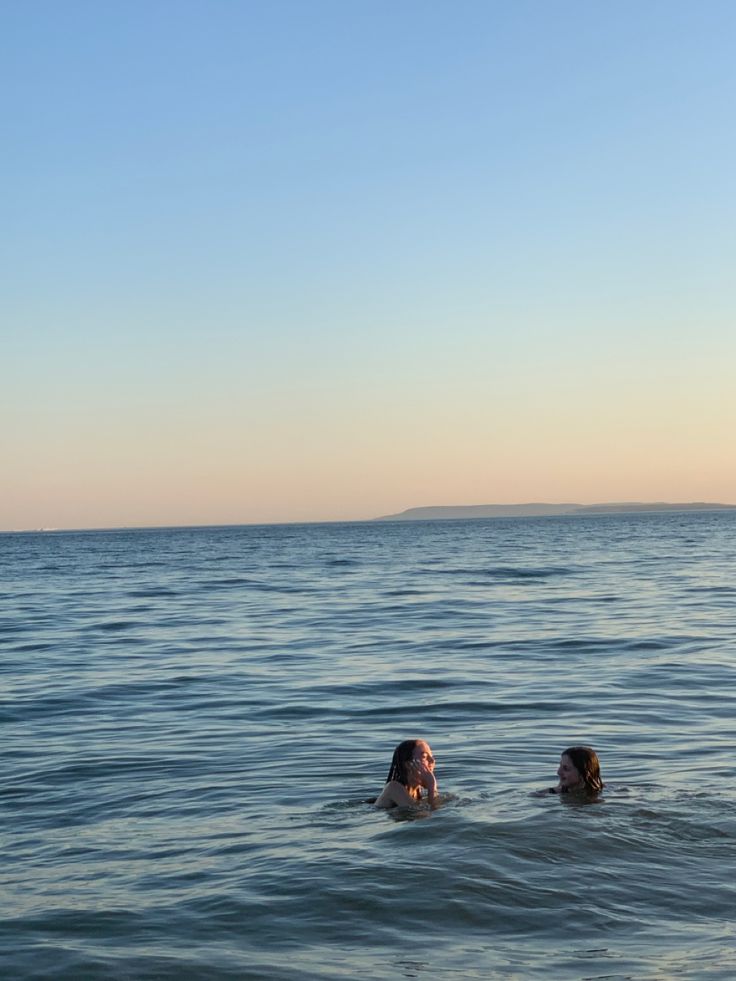 two people swimming in the ocean at sunset