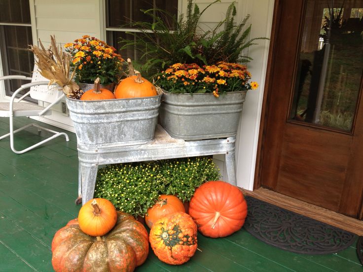 some pumpkins and gourds are sitting on the front porch with flowers in buckets