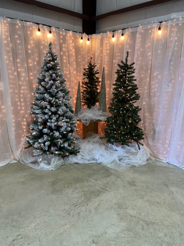 three artificial christmas trees in front of a white curtain