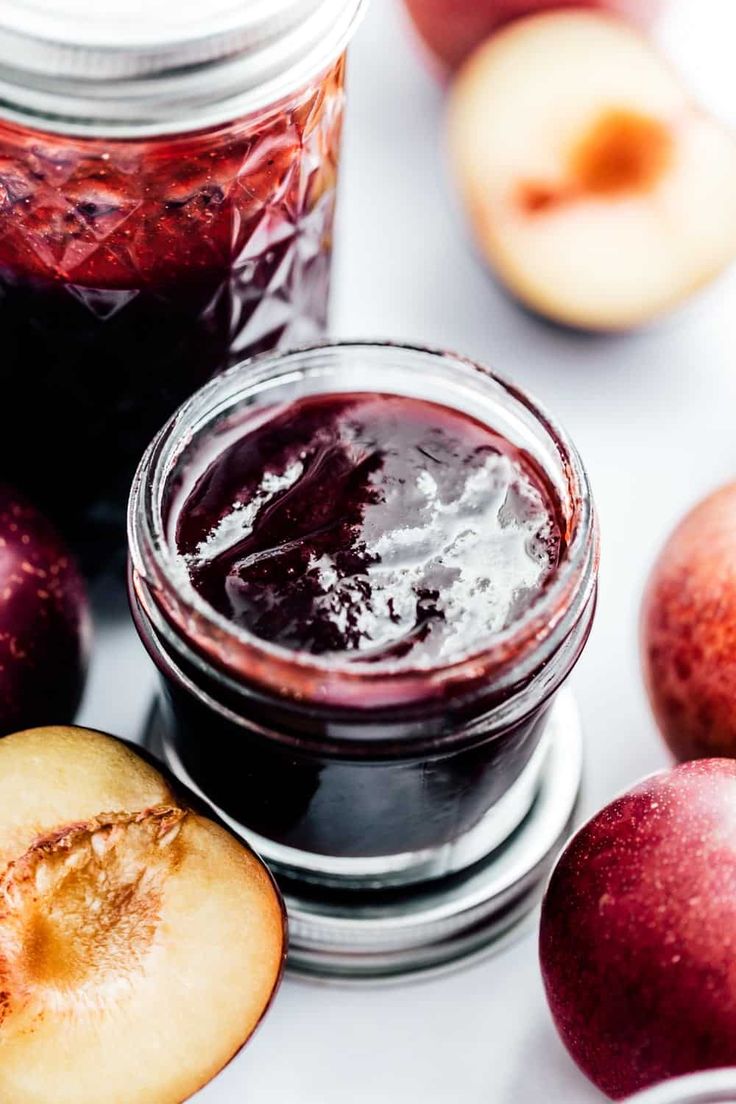 two jars filled with jam next to sliced apples