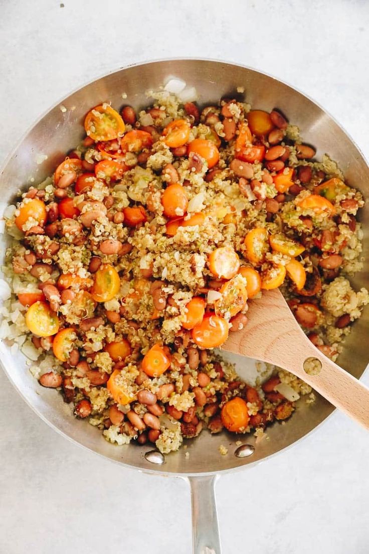 a pan filled with rice and vegetables on top of a white counter next to a wooden spoon