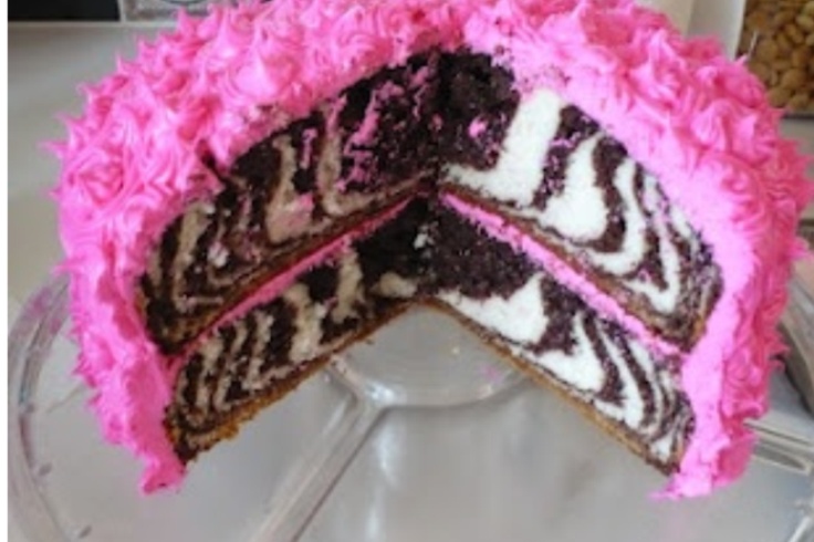 a zebra print cake with pink frosting on a glass platter next to a slice taken out of it