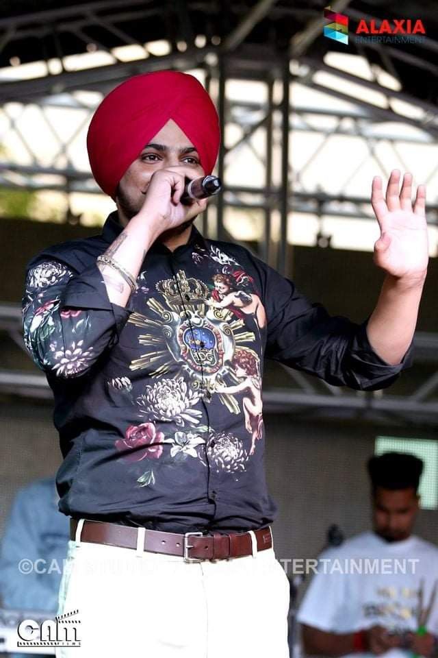 a man with a red turban on his head singing into a microphone at an outdoor event