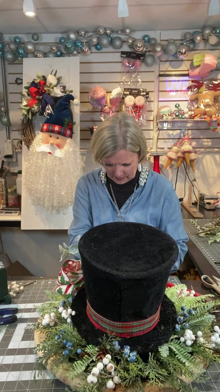 a woman in blue shirt and black hat working on top of a table with decorations