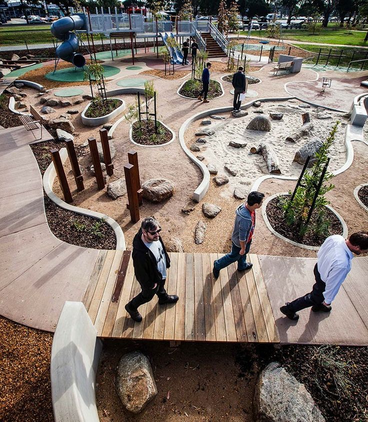 three people walking across a wooden bridge in a park with playgrounds and play areas