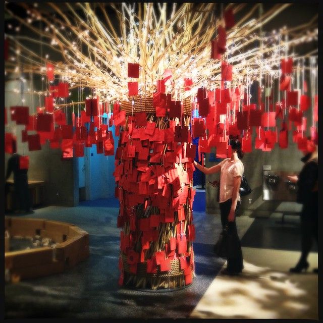 a woman standing next to a tall red sculpture with lots of paper squares on it