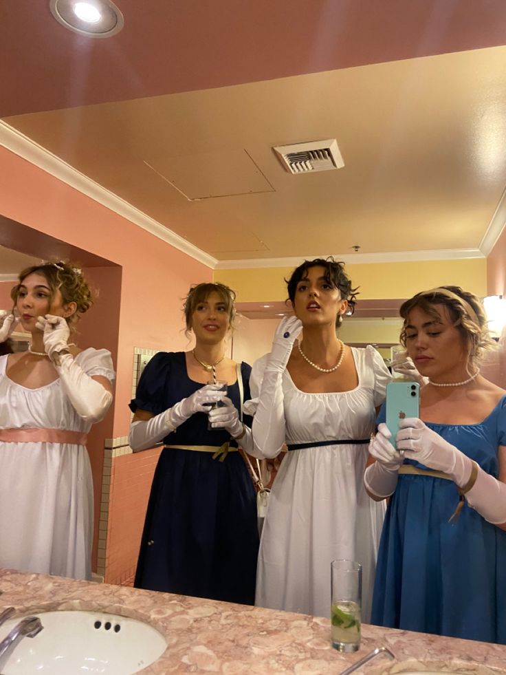 four bridesmaids in dresses are looking at their cell phones as they stand in front of the mirror