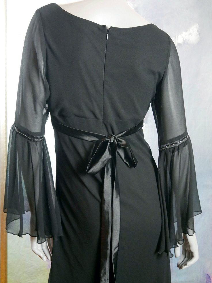 This long black evening dress has a deep V crossover neckline and an empire waistline with a 2-inch (5.08cm) band of silver beading. The fitted waistline gives way to a long A-line skirt with an elegant fall. The long flounce sleeves have a fitted band of silver beading above each elbow. The 1960s style dress (but made in the 1990s) is a sheer crepe polyester fabric, with a black satin polyester lining creating a highly tailored silhouette. A black satin tie belt in the back enables you to fit t Gothic V-neck Evening Dress, Black Empire Waist Evening Dress, 1960s Style Dress, Mad Men Dresses, Long Black Evening Dress, Long A Line Skirt, Formal Cocktail Party, Black Evening Dress, 1960s Style