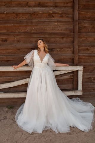 a woman in a wedding dress leaning against a wooden fence with her arms outstretched and hands behind her back