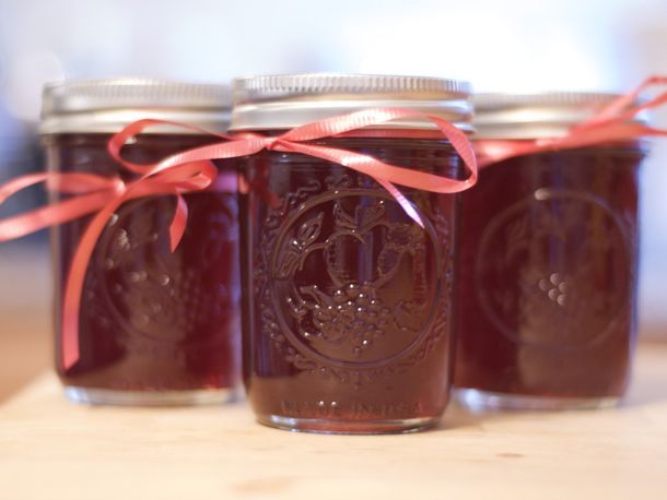 four mason jars with red ribbon tied around the lids, sitting on a wooden table